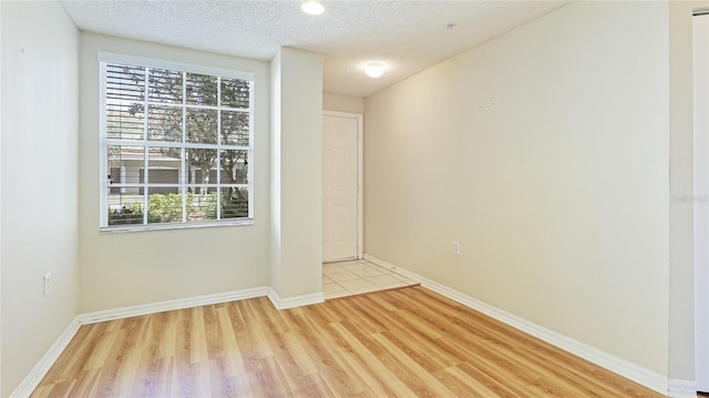 unfurnished room featuring light wood finished floors, a textured ceiling, and baseboards