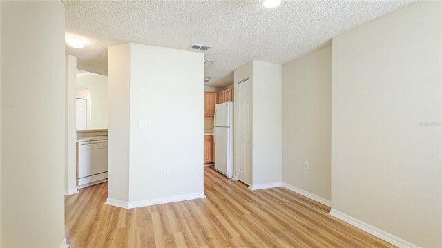 unfurnished room featuring light wood finished floors, visible vents, a textured ceiling, and baseboards