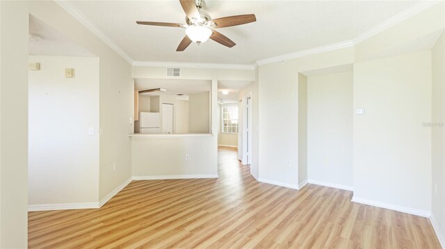 empty room with crown molding, light wood-style flooring, visible vents, and baseboards