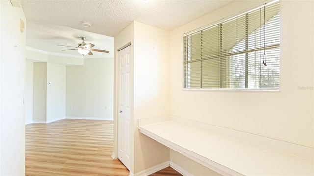 hallway with a textured ceiling, baseboards, and wood finished floors