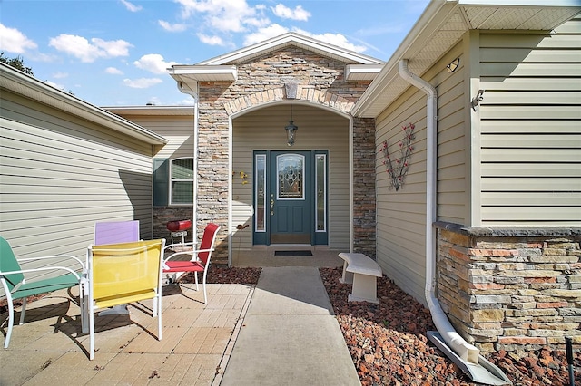 view of exterior entry featuring stone siding and a patio area