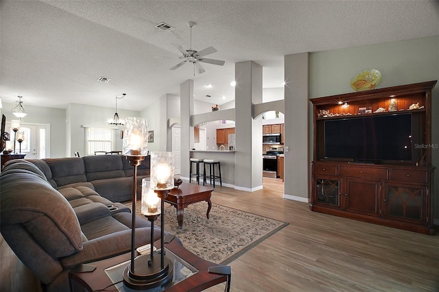 living area featuring a textured ceiling, lofted ceiling, ceiling fan with notable chandelier, visible vents, and light wood finished floors