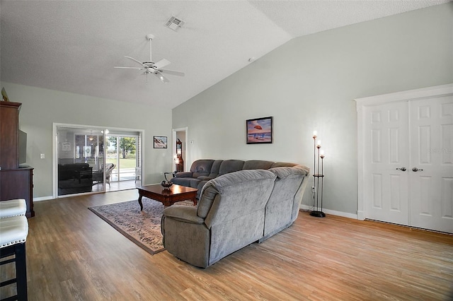 living room featuring high vaulted ceiling, light wood-type flooring, visible vents, and baseboards