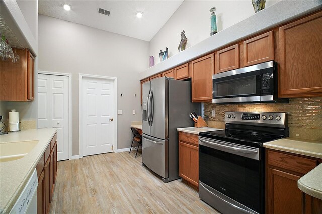 kitchen with stainless steel appliances, light wood finished floors, backsplash, and brown cabinets