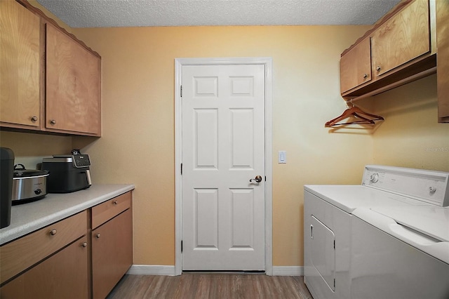 clothes washing area featuring a textured ceiling, washing machine and dryer, baseboards, light wood-style floors, and cabinet space