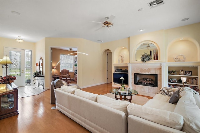 living area with built in shelves, visible vents, a ceiling fan, wood finished floors, and a tile fireplace