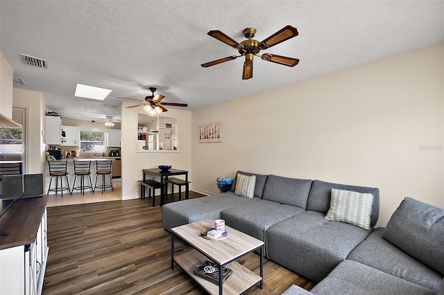 living area with a textured ceiling, a skylight, visible vents, baseboards, and dark wood finished floors