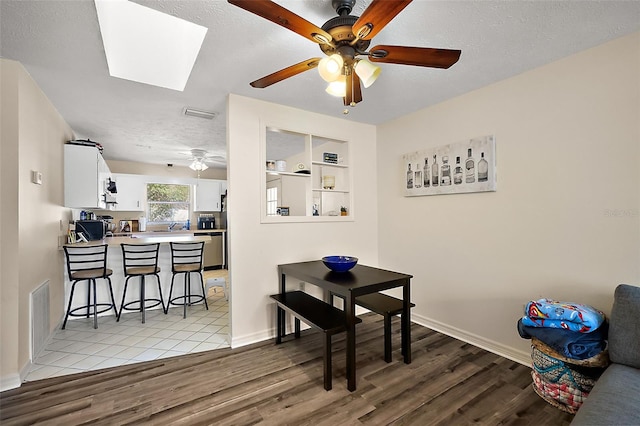 dining area with light wood-style floors, a skylight, a textured ceiling, and baseboards