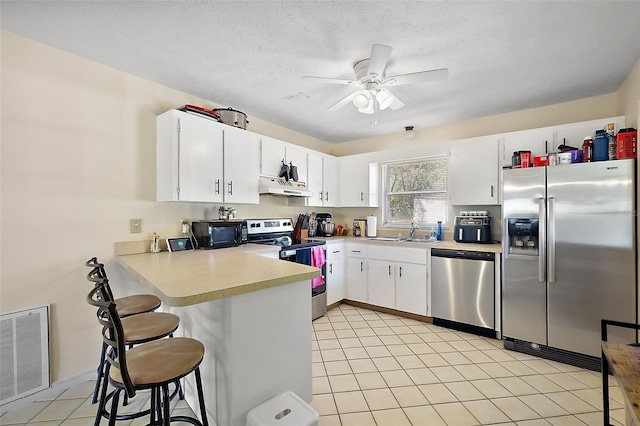 kitchen with under cabinet range hood, stainless steel appliances, a peninsula, visible vents, and light countertops