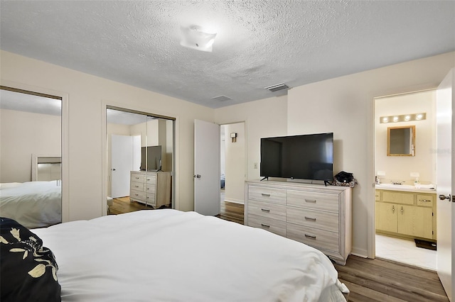 bedroom featuring visible vents, connected bathroom, a textured ceiling, a sink, and wood finished floors