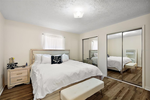 bedroom with a textured ceiling, baseboards, dark wood finished floors, and two closets