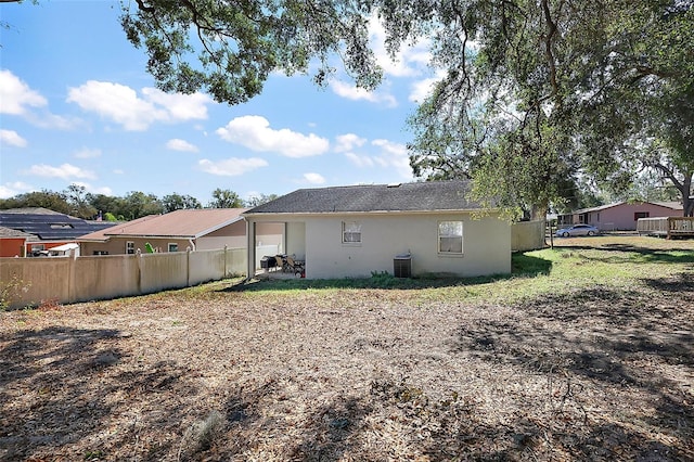 back of house featuring central AC unit, fence, and stucco siding