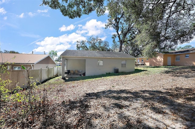 rear view of house with stucco siding, fence, and central air condition unit