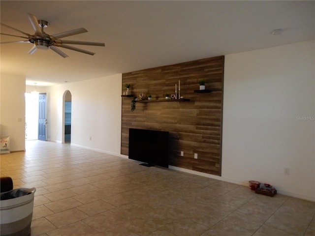 unfurnished living room featuring a ceiling fan, wooden walls, a fireplace, and arched walkways