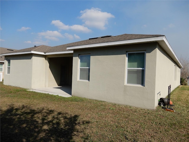 rear view of property featuring stucco siding, a lawn, a patio area, and a shingled roof