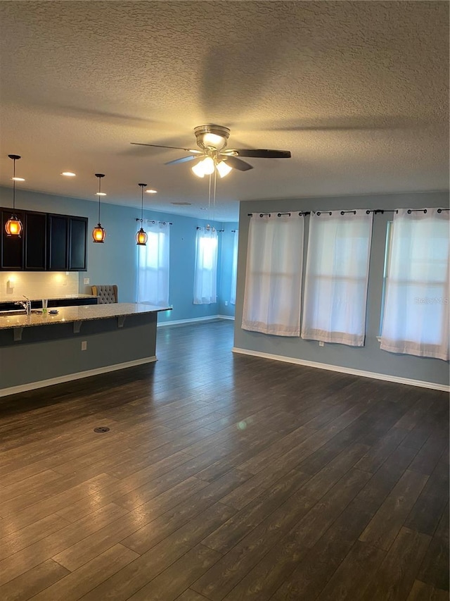 unfurnished living room with dark wood-type flooring, a sink, ceiling fan, and baseboards