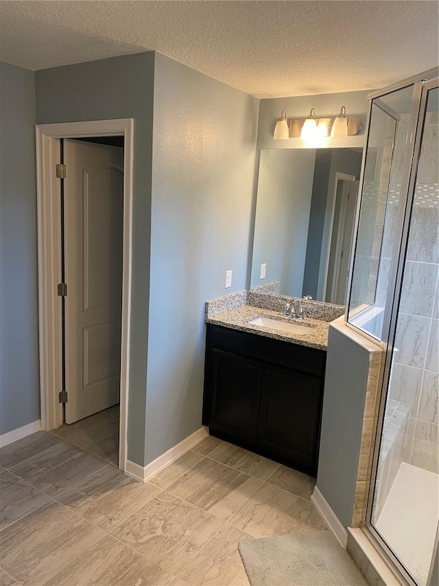 full bath featuring a stall shower, baseboards, vanity, and a textured ceiling