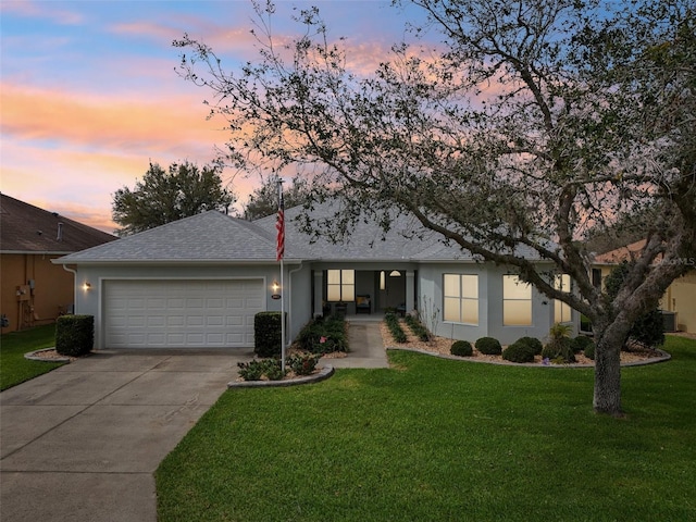 ranch-style house with roof with shingles, stucco siding, concrete driveway, a garage, and a front lawn