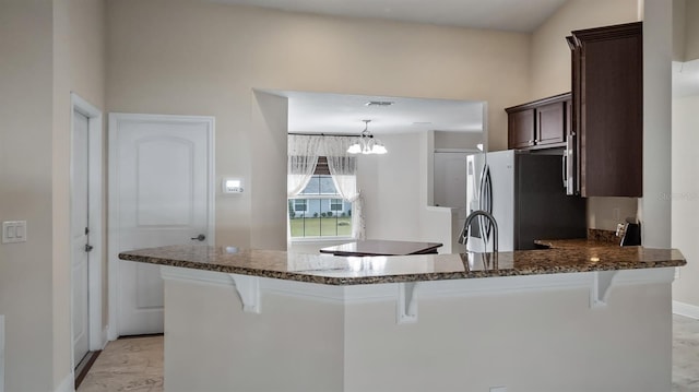 kitchen with dark stone counters, dark brown cabinets, a breakfast bar area, and freestanding refrigerator