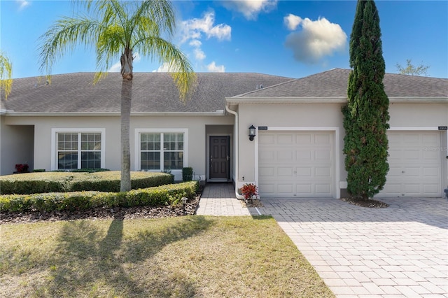 ranch-style home featuring a garage, decorative driveway, roof with shingles, and stucco siding