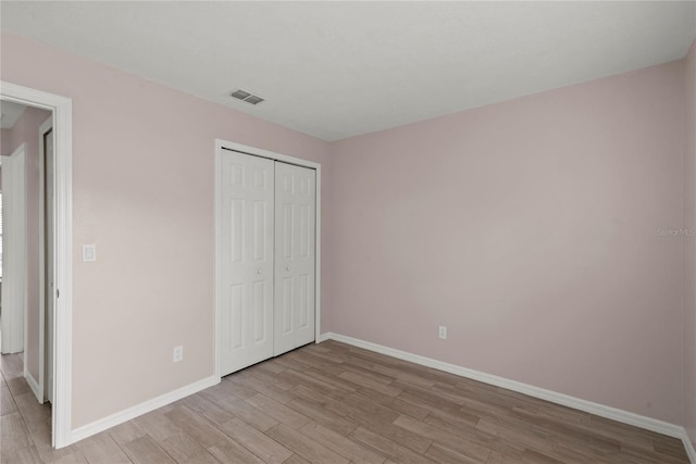 unfurnished bedroom featuring light wood-style floors, a closet, visible vents, and baseboards