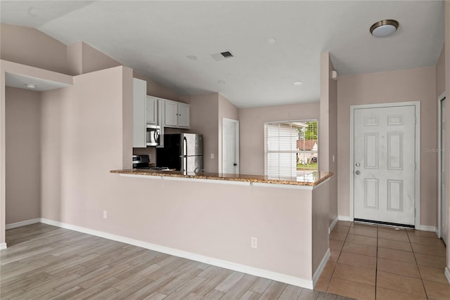 kitchen with visible vents, appliances with stainless steel finishes, stone countertops, white cabinets, and vaulted ceiling