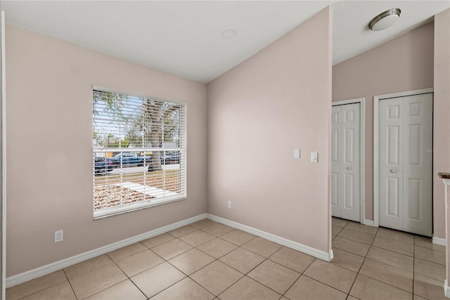 spare room featuring light tile patterned floors, vaulted ceiling, and baseboards