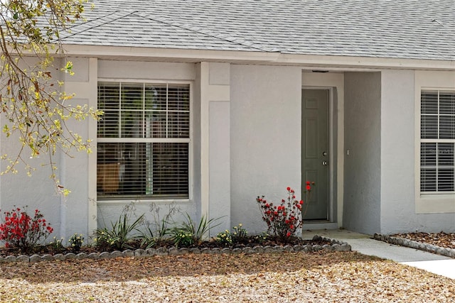 view of exterior entry featuring roof with shingles and stucco siding