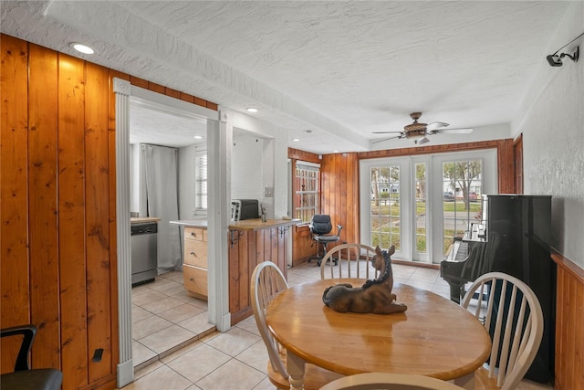 dining room with wooden walls, ceiling fan, a textured ceiling, and light tile patterned floors