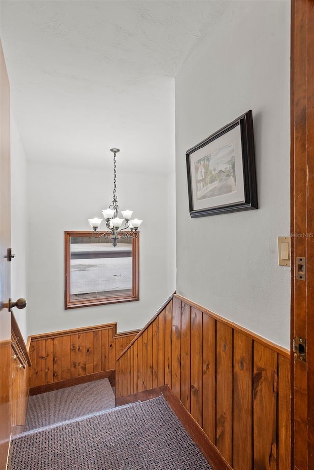 interior space with wood walls, carpet, a notable chandelier, and wainscoting