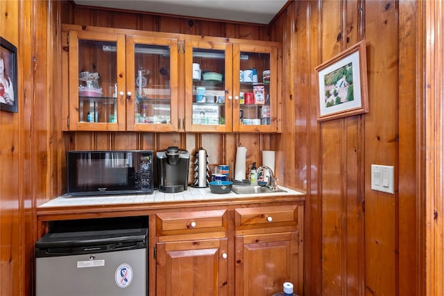 bar with black microwave, a sink, wooden walls, and fridge