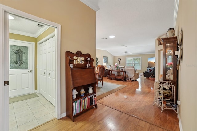 corridor featuring baseboards, visible vents, lofted ceiling, light wood-style flooring, and ornamental molding