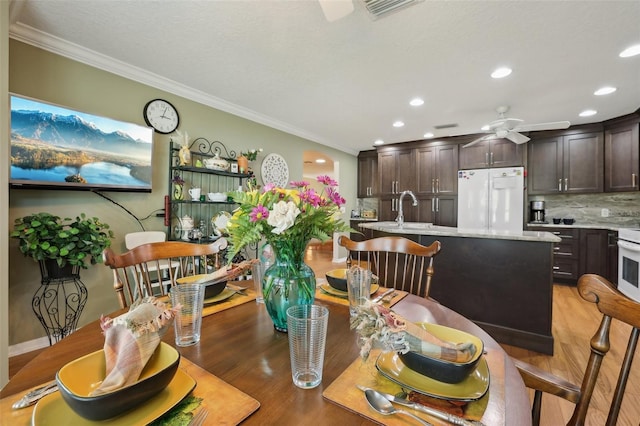 dining area with ceiling fan, light wood-type flooring, visible vents, and ornamental molding