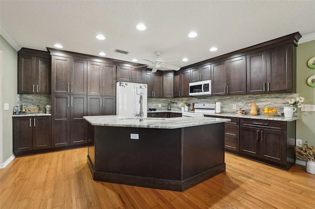 kitchen featuring white appliances, visible vents, a sink, dark brown cabinetry, and light wood-style floors