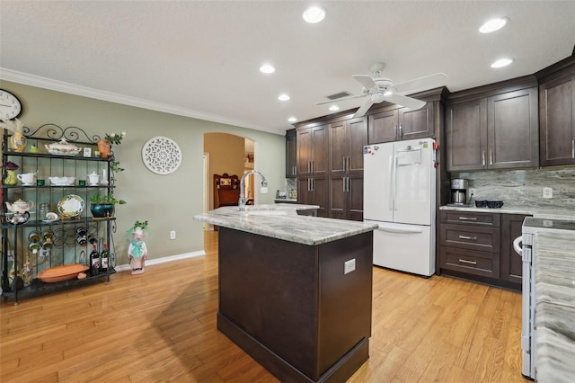 kitchen with white appliances, arched walkways, dark brown cabinets, and a center island with sink