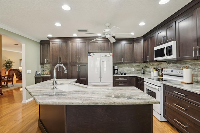 kitchen featuring white appliances, visible vents, an island with sink, arched walkways, and a sink