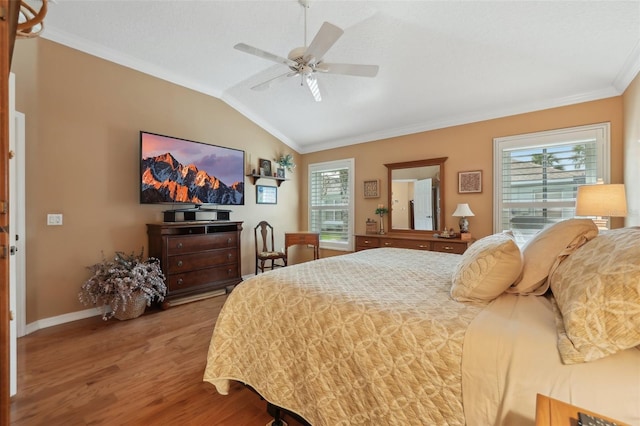 bedroom featuring a ceiling fan, wood finished floors, baseboards, vaulted ceiling, and crown molding