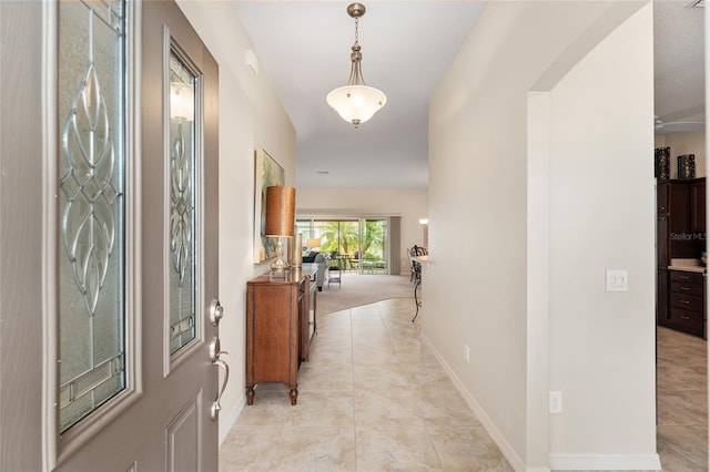 foyer featuring light tile patterned floors, baseboards, and arched walkways