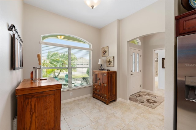 foyer featuring arched walkways, light tile patterned flooring, and baseboards