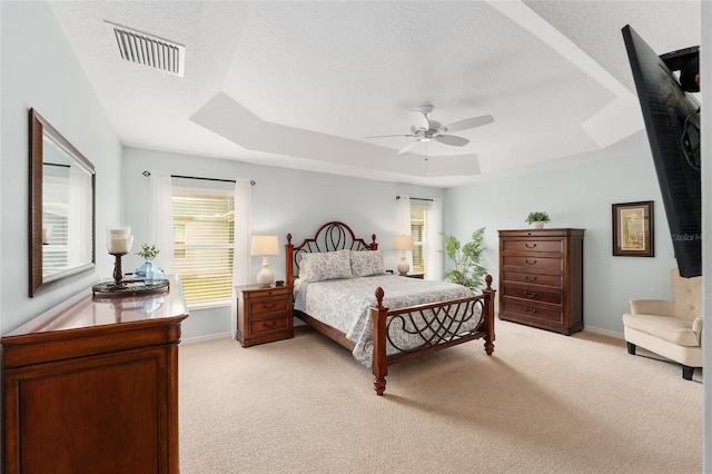 bedroom with baseboards, visible vents, light colored carpet, a tray ceiling, and a textured ceiling