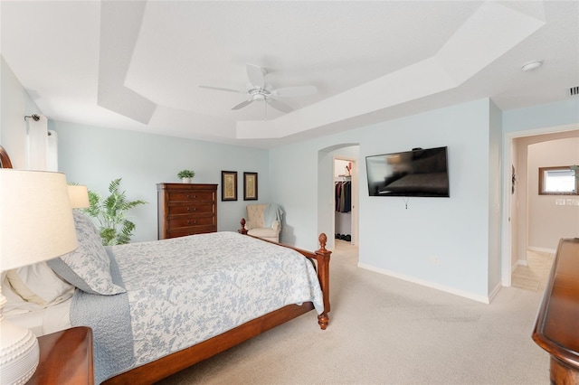 bedroom with arched walkways, a raised ceiling, light colored carpet, a spacious closet, and a ceiling fan