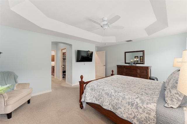 carpeted bedroom with arched walkways, visible vents, baseboards, a raised ceiling, and a walk in closet