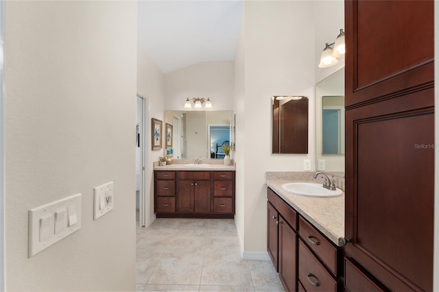 bathroom with baseboards, lofted ceiling, tile patterned floors, a sink, and two vanities