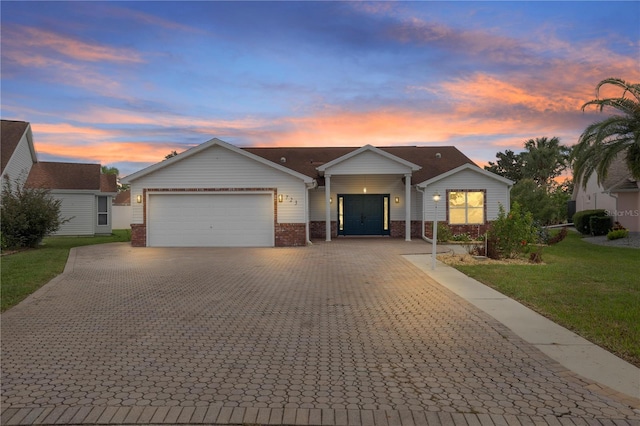 ranch-style home with brick siding, a lawn, an attached garage, and decorative driveway