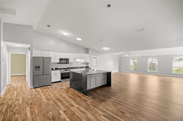 kitchen with a center island, dark countertops, appliances with stainless steel finishes, open floor plan, and white cabinetry