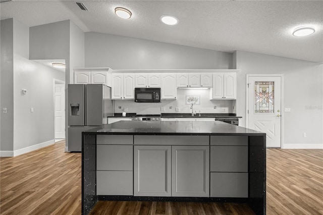 kitchen featuring black microwave, dark countertops, stainless steel fridge, and white cabinetry