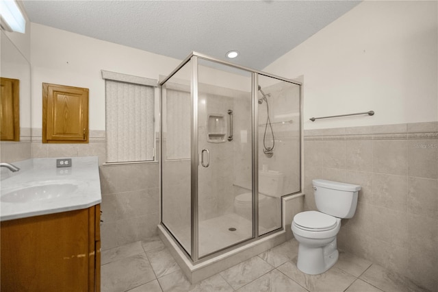 bathroom with tile walls, toilet, a shower stall, a textured ceiling, and vanity