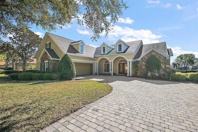 view of front of property with decorative driveway, stone siding, a front lawn, and stucco siding