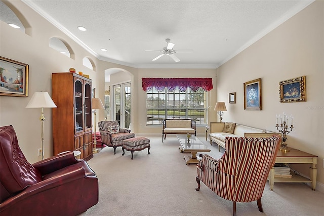 carpeted living room featuring baseboards, arched walkways, a ceiling fan, ornamental molding, and a textured ceiling