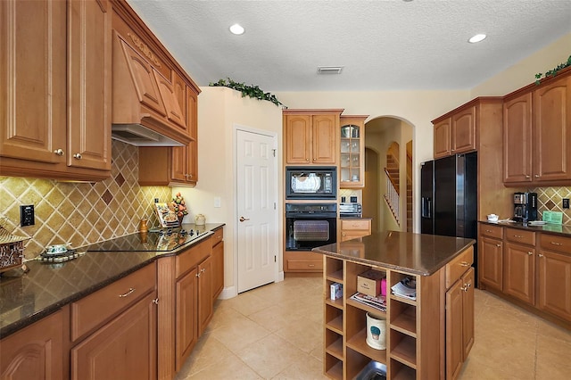 kitchen with arched walkways, open shelves, a kitchen island, black appliances, and glass insert cabinets